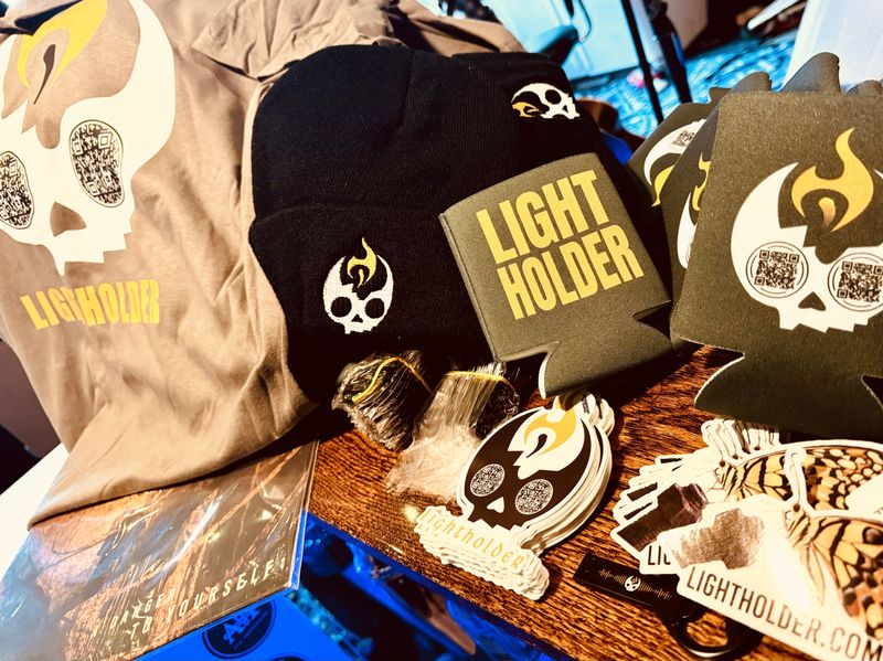 Lightholder merch — t-shirts, beanies, koozies and stickers on a merch table